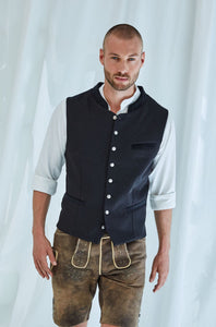 Die markante Weste aus der Goldhirsch X RETLA e.V. Kollektion überzeugt mit dezent gemustertem Schwarz und edlen Samtdetails an Kragen und Taschen.