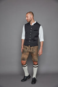 Die markante Weste aus der Goldhirsch X RETLA e.V. Kollektion überzeugt mit dezent gemustertem Schwarz und edlen Samtdetails an Kragen und Taschen.